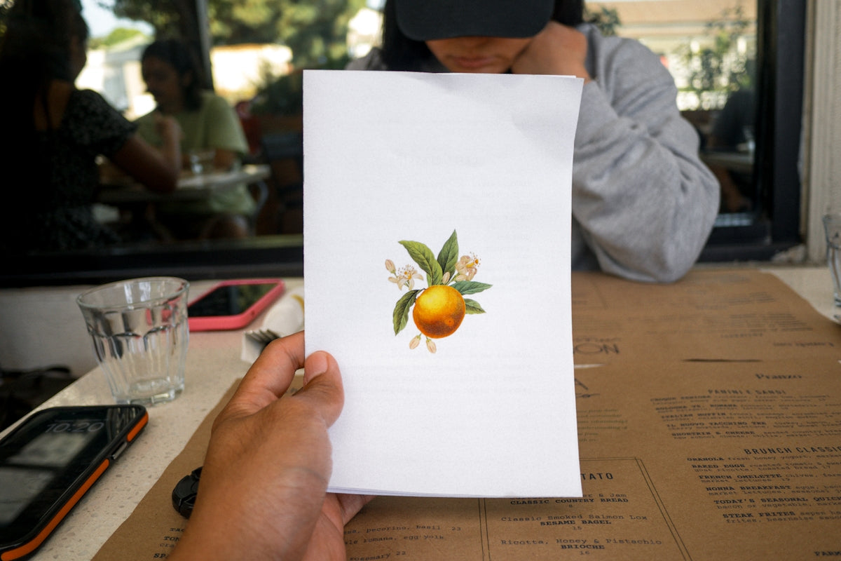 Hand holding a paper with an orange and leaves design.