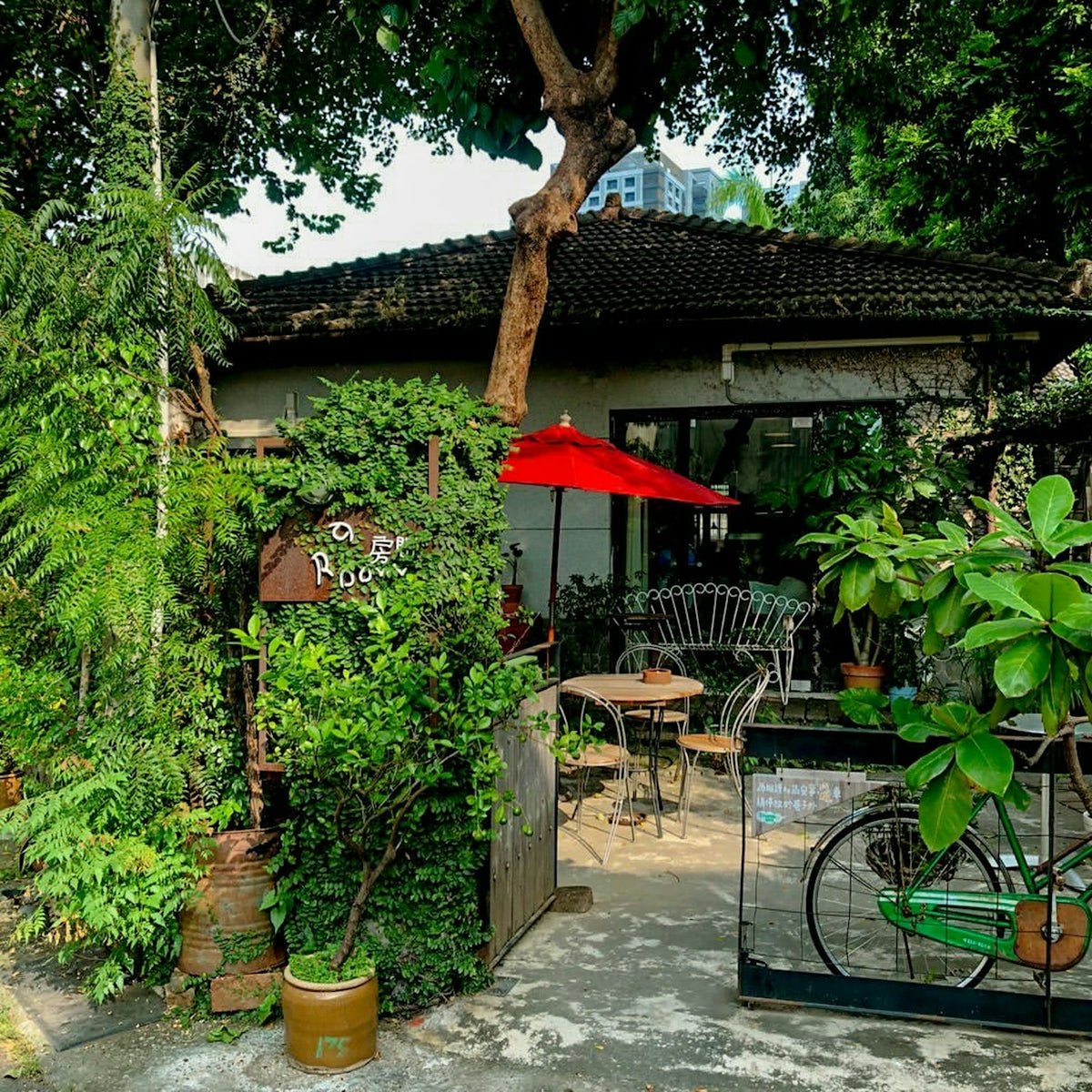 A small cafe patio with a red umbrella, metal chairs, and a green bicycle